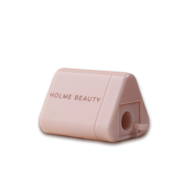 A pink ergonomic pencil sharpener with a triangular container and the brand 'HOLME BEAUTY' printed on the side.