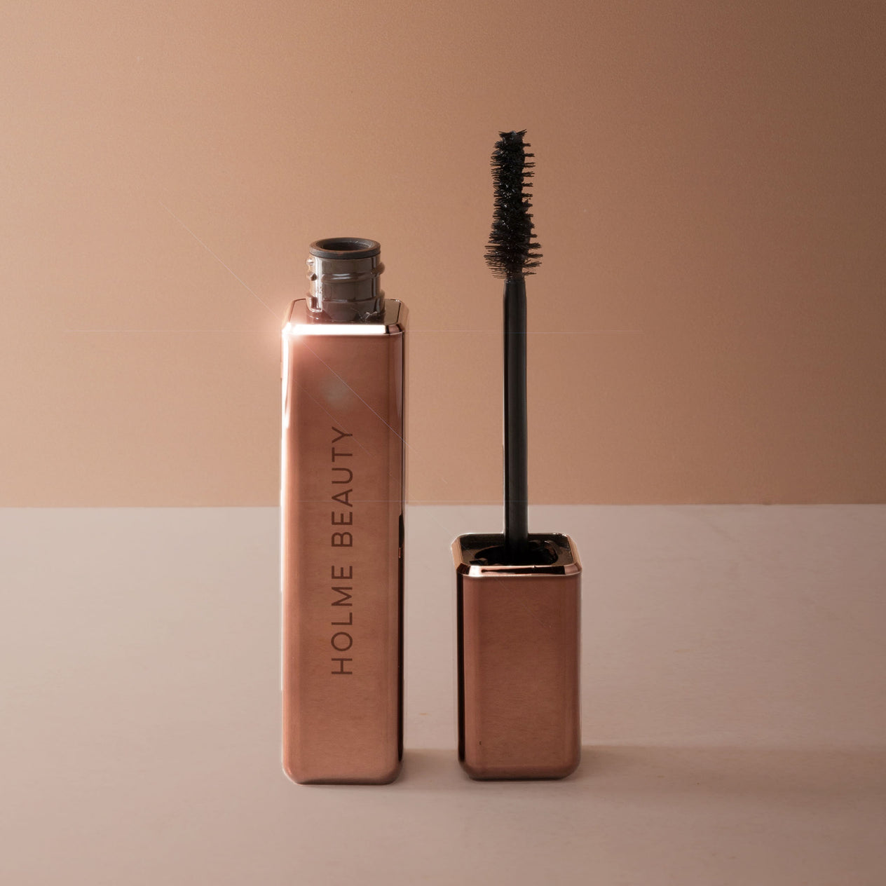Bronze mascara with brush on a beige background, featuring the brand 'Holme Beauty'.